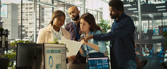 Portrait of smiling coworkers looking over revenue figures on paperwork in office. Happy team of accountants focused on comparing company statistical numbers to finish job before deadline, camera B